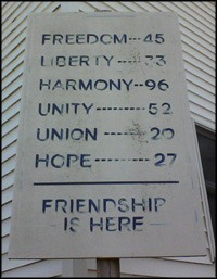 a sign on the corner of a building reading, Freedom-45, Liberty-33, Harmony-96, Unity-52, Union 26, Hope-27, Friendship is Here