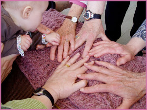 the hands of a baby and a group of women rest in a circle on a pink crocheted blanket