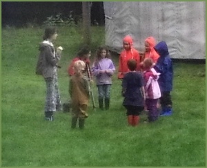 a teacher and a group of students meet in a circle, outdoors on a rainy day