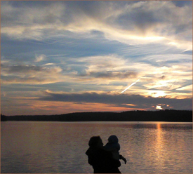 a mother holding a child in her arms silhouetted against the background of a river and sunset