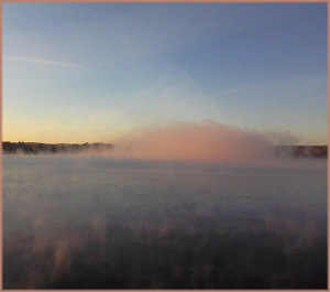 a cloud of rosy colored mist rises from the river at sunrise